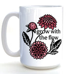A white ceramic mug with a floral design featuring pink and black flowers and the text "grow with the flow" printed on it.