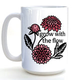 A white ceramic mug with a floral design featuring pink and black flowers and the text "grow with the flow" printed on it.