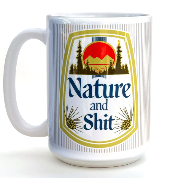 A white ceramic mug with a graphic design featuring a mountain landscape, pine trees, and a red sun. The text on the mug reads "Nature and Shit".
