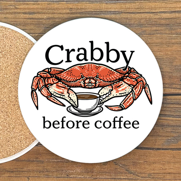 A white coaster with a red crab and a cup of coffee, accompanied by the text "Crabby before coffee".
