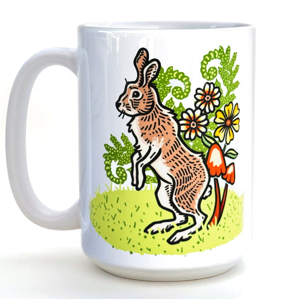 A white ceramic mug with a colorful illustration of a rabbit or hare standing on a grassy area with flowers and mushrooms.