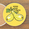 A yellow coaster with a cartoon illustration of two zucchini and the text "eyes up here" on it.