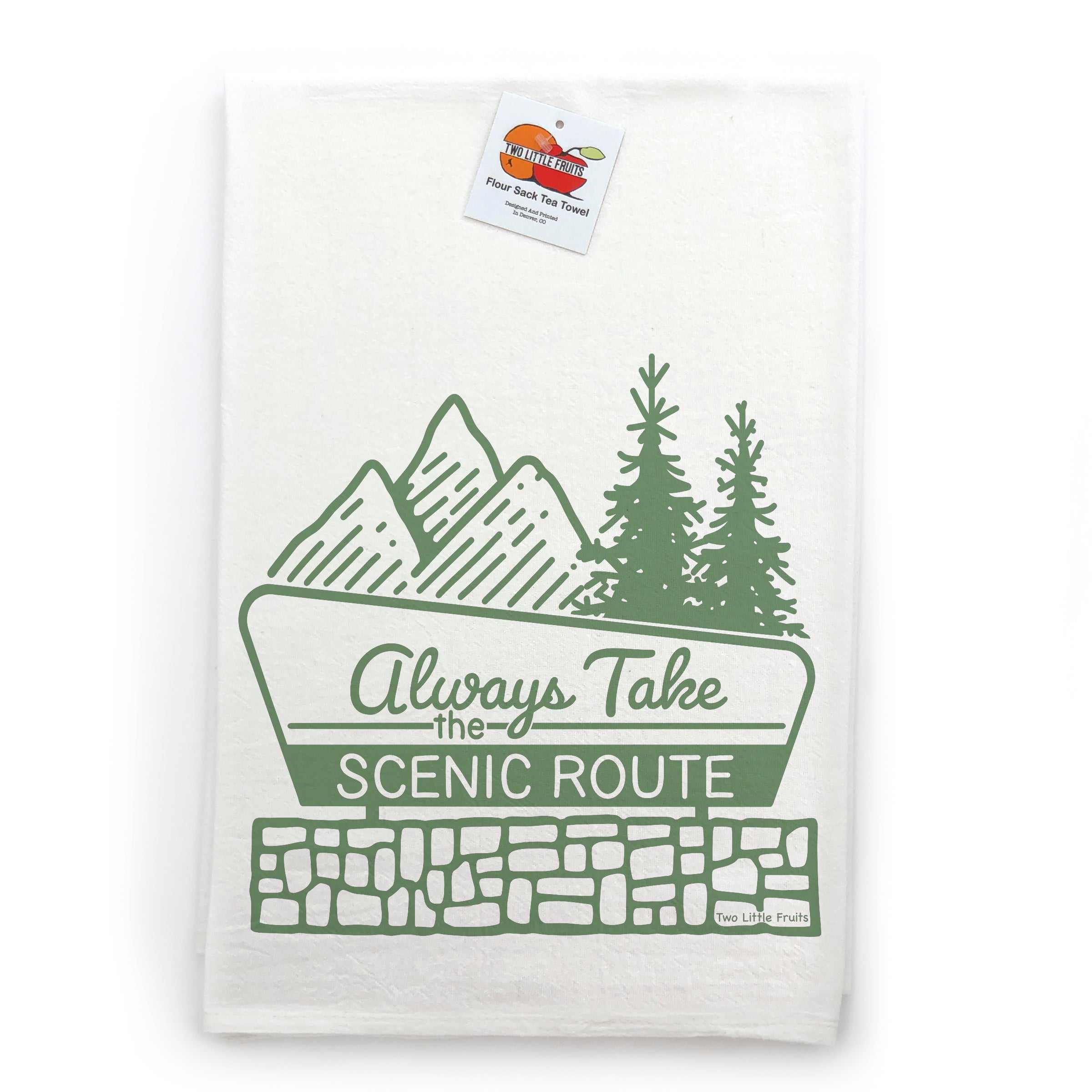 A white towel with a green graphic design depicting mountains, pine trees, and the text "Always Take the Scenic Route" printed on it.