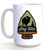 A white ceramic mug with a graphic design featuring a bison silhouette and the text "Stay Wild" inside an arrow-shaped emblem.