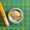 Close-up of the back of the Chicken Button Pin 'Fresh Outta Clucks', with a pencil for scale, highlighting the lightweight design of this funny chicken pin.