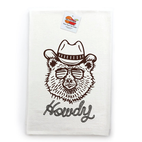 An image showcasing a cowboy bear kitchen towel, displaying a charming design of a bear in sunglasses and a cowboy hat on a white background. The towel is neatly folded with a tag indicating it is a flour sack tea towel, adding a fun touch to any kitchen decor.