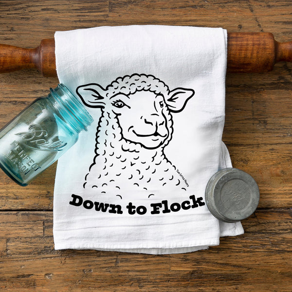 Adorable lamb print kitchen towel displaying a cheerful sheep with the phrase 'Down to Flock' on a wooden surface beside mason jars.