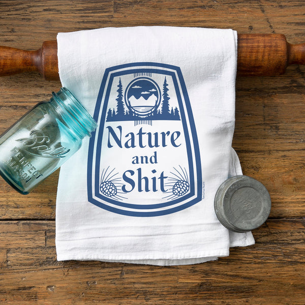 Nature and Sh*t cotton tea towel used as ironic kitchen decor, featuring a playful design with mountains and trees on a white towel, perfect for adding humor to your kitchen.