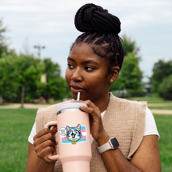 A joyful person sipping from a cup featuring the Protect Transgender Youth Cat Sticker, which boldly states 'Purrtect Trans Youth!' This vibrant sticker represents transgender youth support stickers and promotes LGBTQ PRIDE. A fun and new way to show your support!