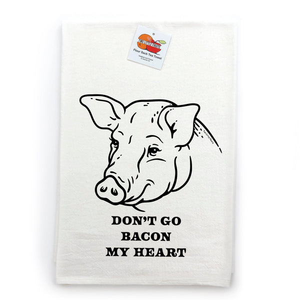 A neatly folded cotton tea towel showcasing a whimsical pig illustration and the caption 'DON'T GO BACON MY HEART.' The towel is tagged with the brand name and set against a white background.