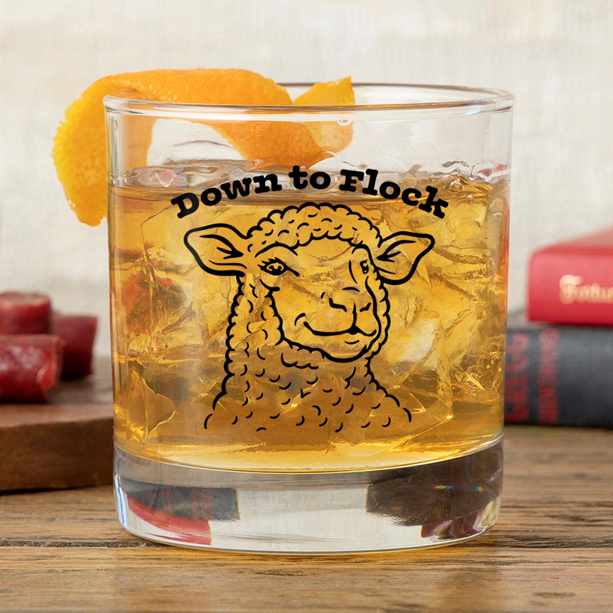 Funny Lamb Whiskey Glass with a drink and orange peel garnish, featuring a playful lamb illustration and the text 'Down to Flock'.