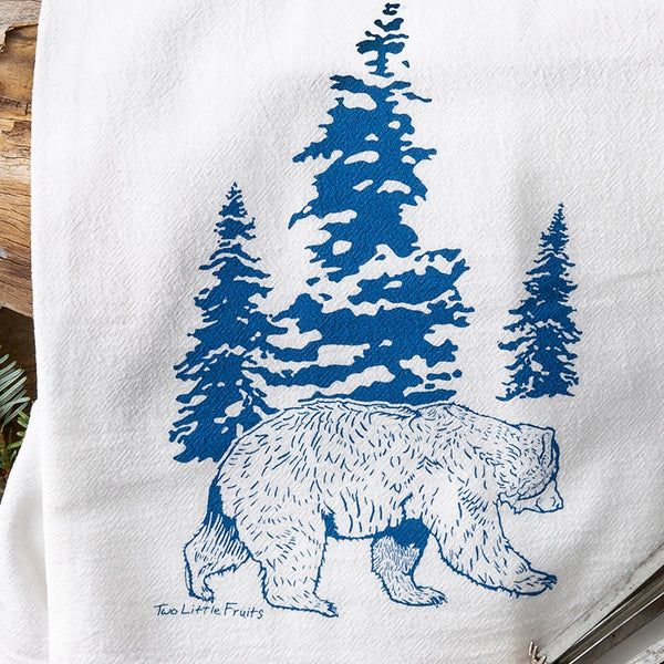 Close-up of a bear kitchen towel featuring a hand-drawn royal blue bear design with evergreen trees against a white background.