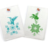 Bright display of Two Little Fruits kitchen towels showing a blue hummingbird and a green bee, neatly stacked and tagged on a clean white background.