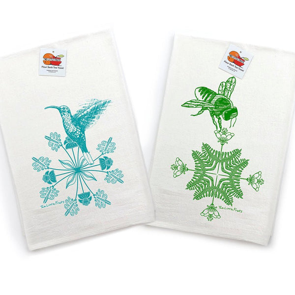 Bright display of Two Little Fruits kitchen towels showing a blue hummingbird and a green bee, neatly stacked and tagged on a clean white background.