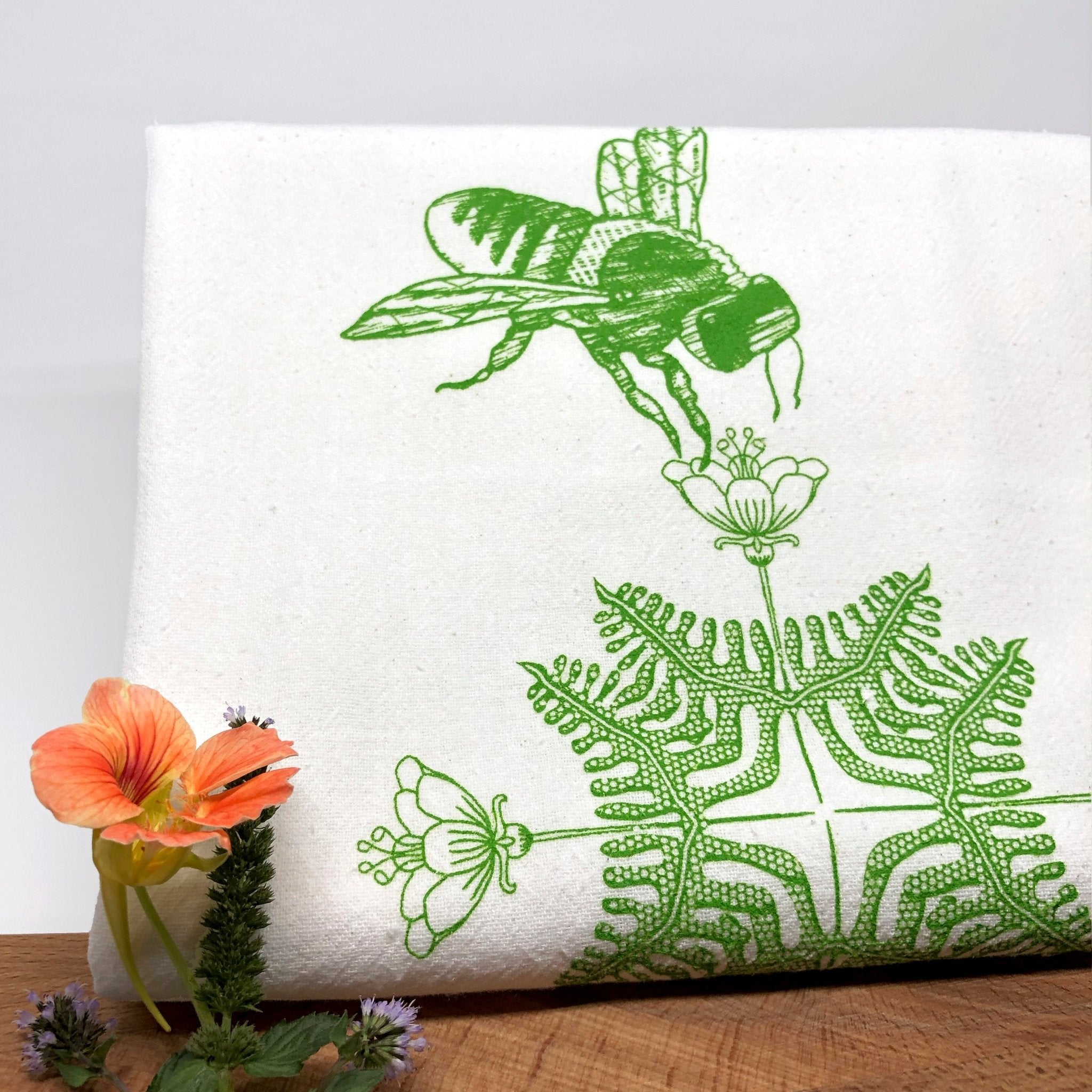 Creative tea towel design with a green bee and fern flower illustration, highlighting unique tea towel designs for an eco-friendly kitchen.