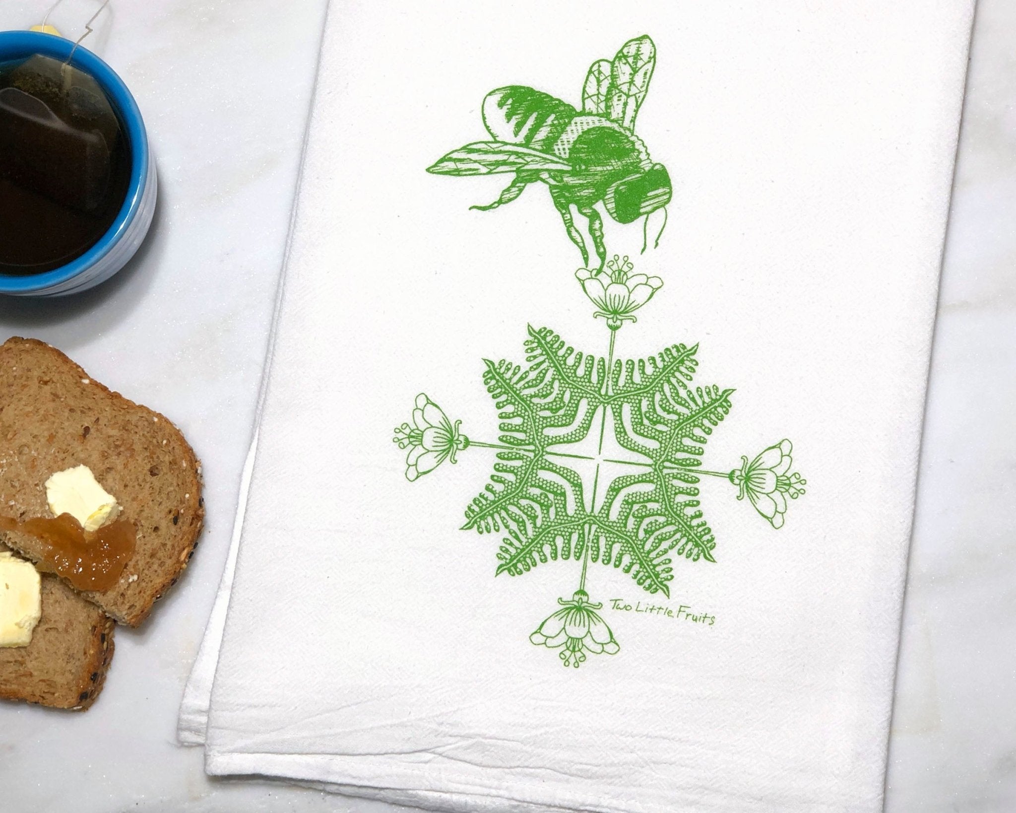 Stylish tea towel featuring a green bee and floral motif, representing unique tea towel designs that brighten up any culinary space.