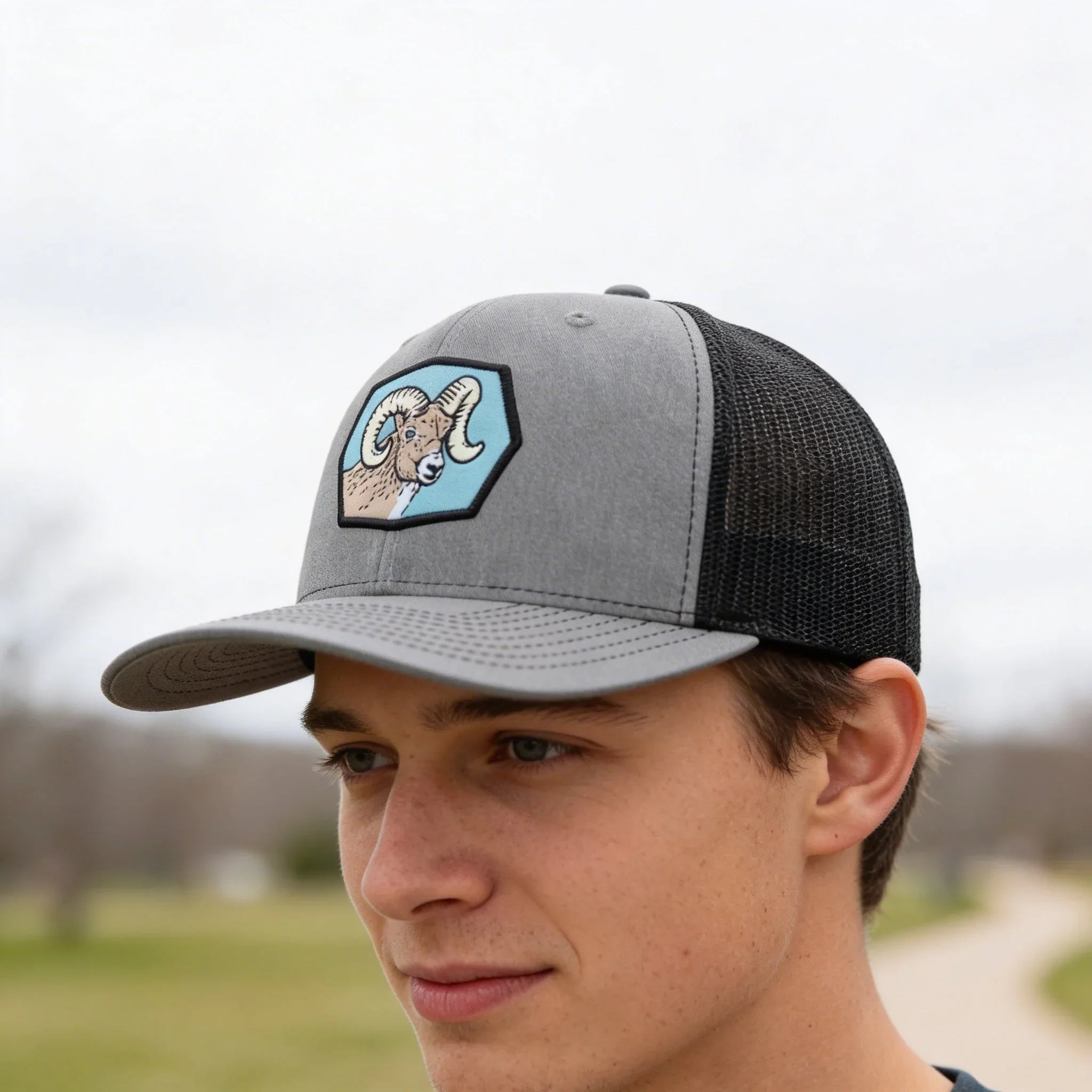 A young man wearing a gray baseball cap with a blue and white graphic of a ram on it, looking off to the side.