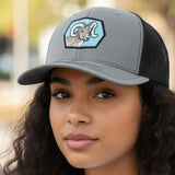 A young woman with long curly hair wearing a gray baseball cap with a graphic of a ram on it.