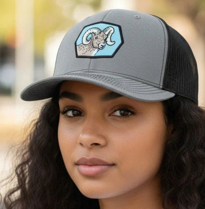 A young woman with long curly hair wearing a gray baseball cap with a graphic of a ram on it.