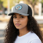 A young woman with long curly hair wearing a gray baseball cap with a graphic of a ram on it.