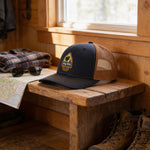 a wooden bench with a black baseball cap with a mesh front, a pair of sunglasses, a map, and a pair of boots.