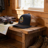 a wooden bench with a black baseball cap with a mesh front, a pair of sunglasses, a map, and a pair of boots.