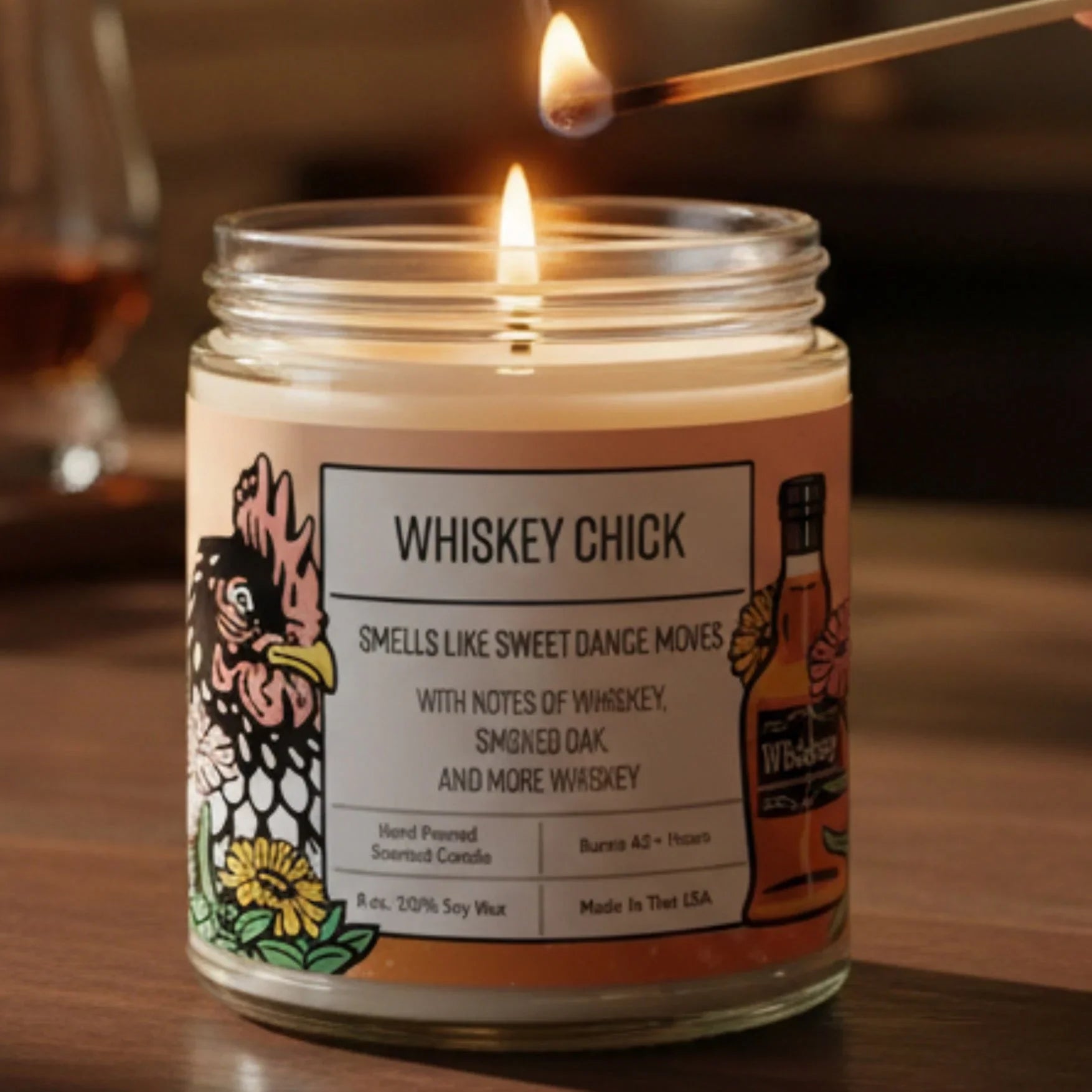 A hand is lighting a candle labeled "Whiskey Chick" on a wooden surface, with several glasses of whiskey in the background.