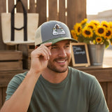 A man wearing a gray baseball cap with a logo is smiling and looking to the side.