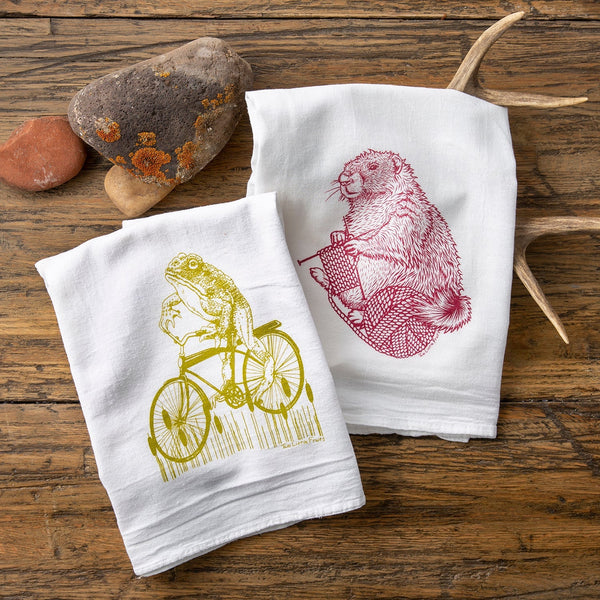 Frog and Marmot Tea Towel Set featuring a hand-illustrated moss green frog on a vintage bicycle and a raspberry knitting marmot, perfect as unique tea towel gifts.