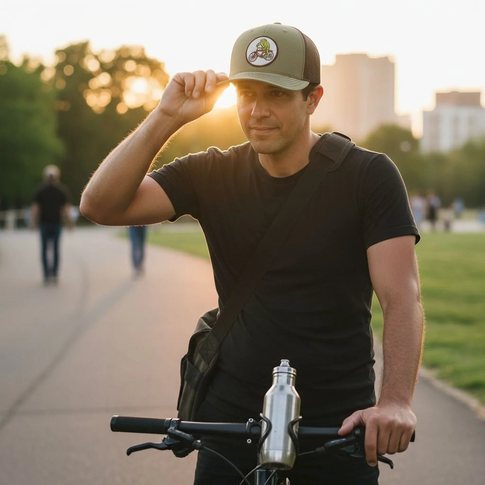 A man wearing a green baseball cap and a black shirt is riding a bicycle on a path, with a backpack on his back.