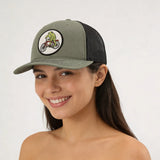 A woman wearing a green baseball cap with a cartoon image of a person riding a bicycle on it.