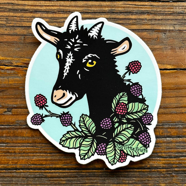 Cheerful Goat Laptop Sticker featuring a black goat with yellow eyes surrounded by vibrant blackberries and green leaves. Perfect for adding a fun touch to your belongings! Ideal choice among goat laptop stickers by Two Little Fruits.