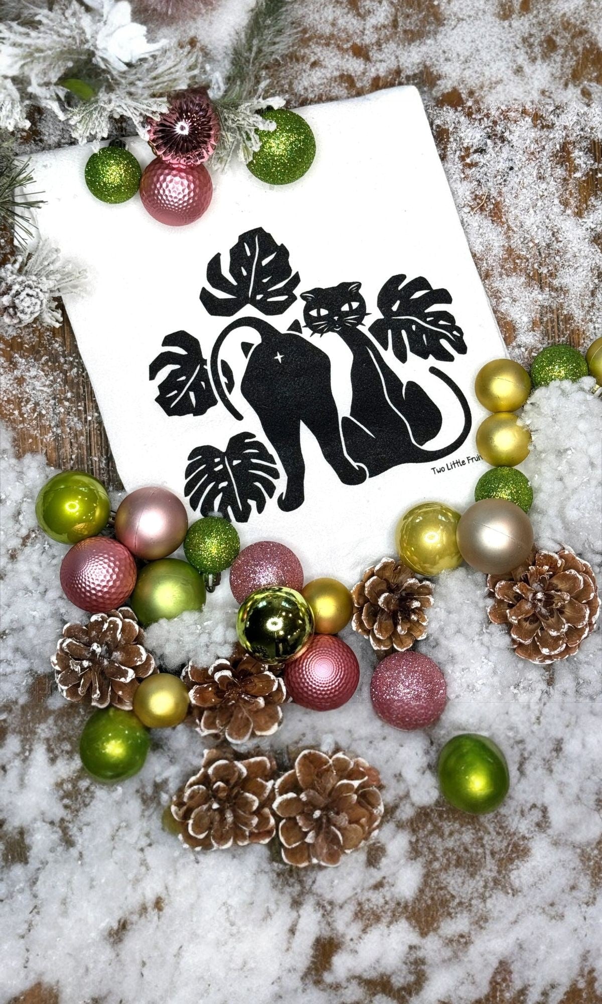 Black cat tea towel with pinecones and ornaments in snow