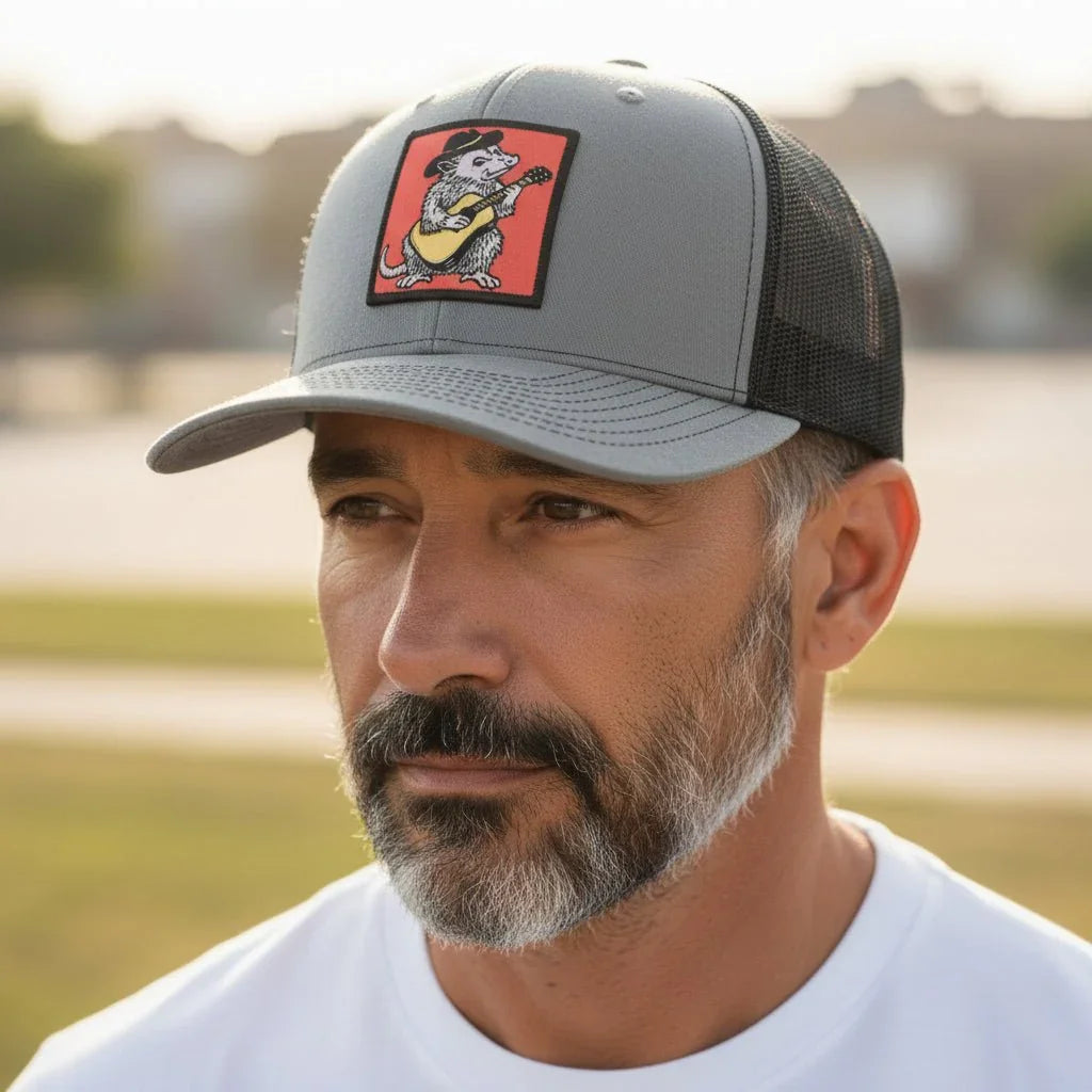 A man wearing a gray baseball cap with a cartoon image of a cat playing a guitar on it.