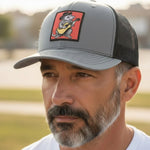 A man wearing a gray baseball cap with a cartoon image of a cat playing a guitar on it.