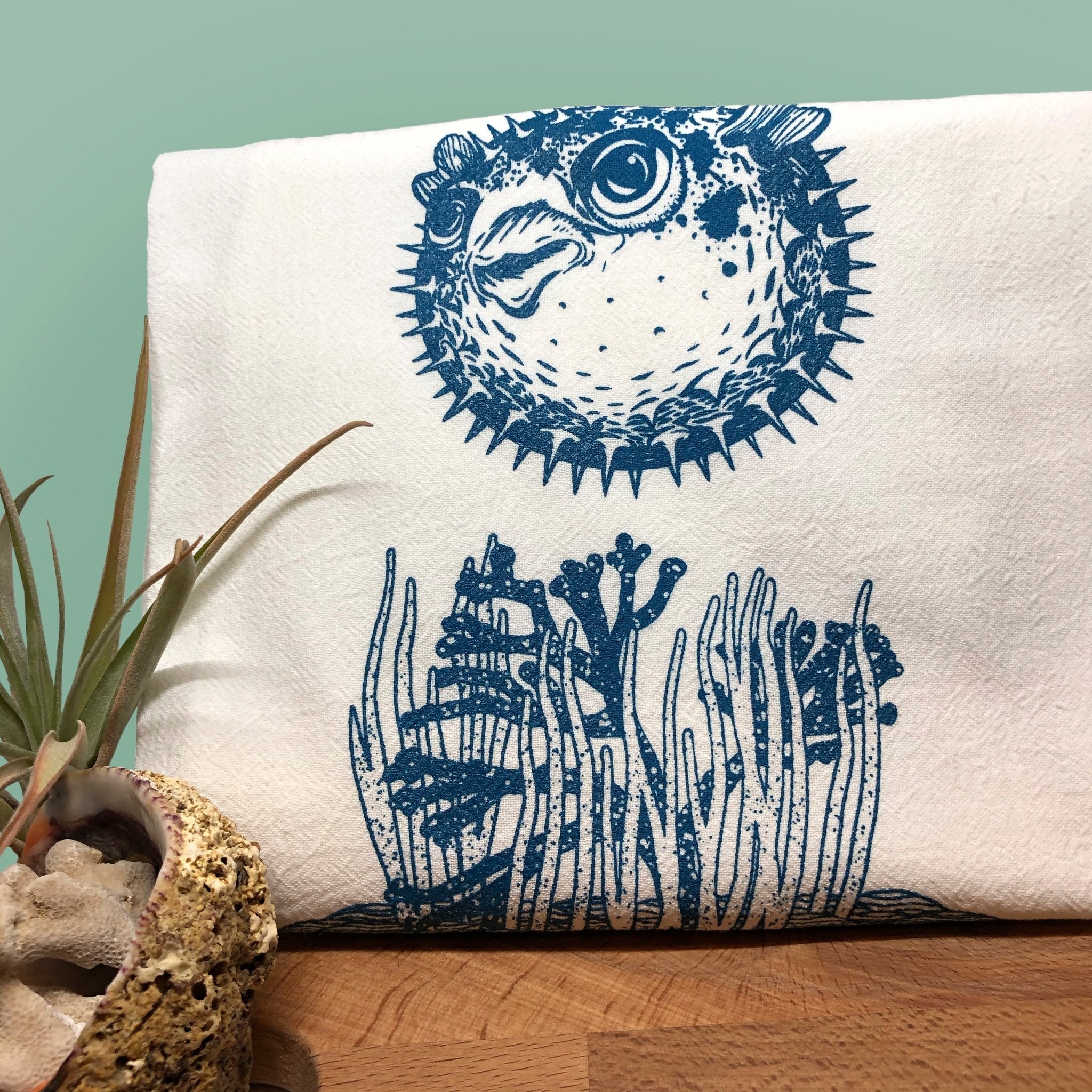 Charming pufferfish tea towel featuring a playful illustration of a blue pufferfish above ocean plants, ideal for adding joy to kitchen chores.
