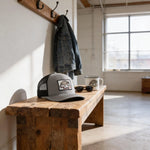 a wooden bench with a gray baseball cap, sunglasses, and a mug with a bear design on it, placed on a wooden coat rack.