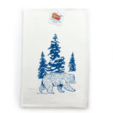Close-up of a bear kitchen towel displaying a blue bear graphic walking among green pine trees, set against a white background.