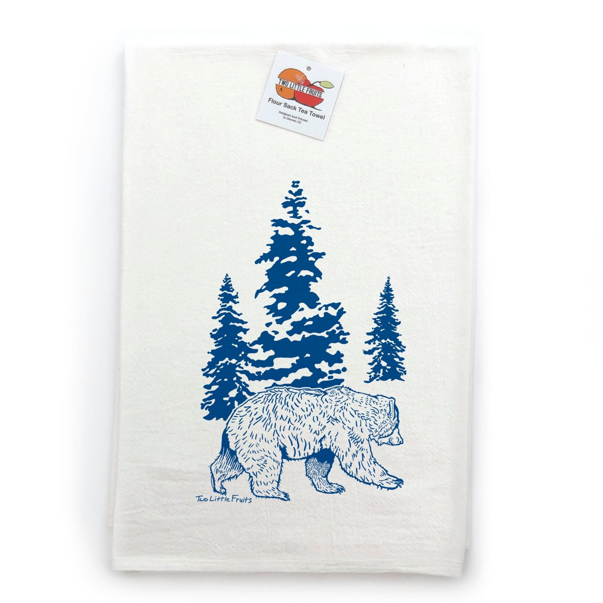 Close-up of a bear kitchen towel displaying a blue bear graphic walking among green pine trees, set against a white background.