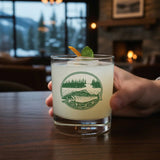 A hand is holding a glass containing a cocktail garnished with a lime and a sprig of mint.