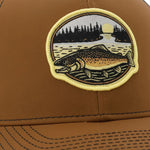 A close-up of a brown baseball cap with a patch featuring a fish and a landscape scene.