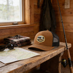 a brown baseball cap with a nature-themed patch, a pair of sunglasses, a map, and a fishing rod on a wooden surface.