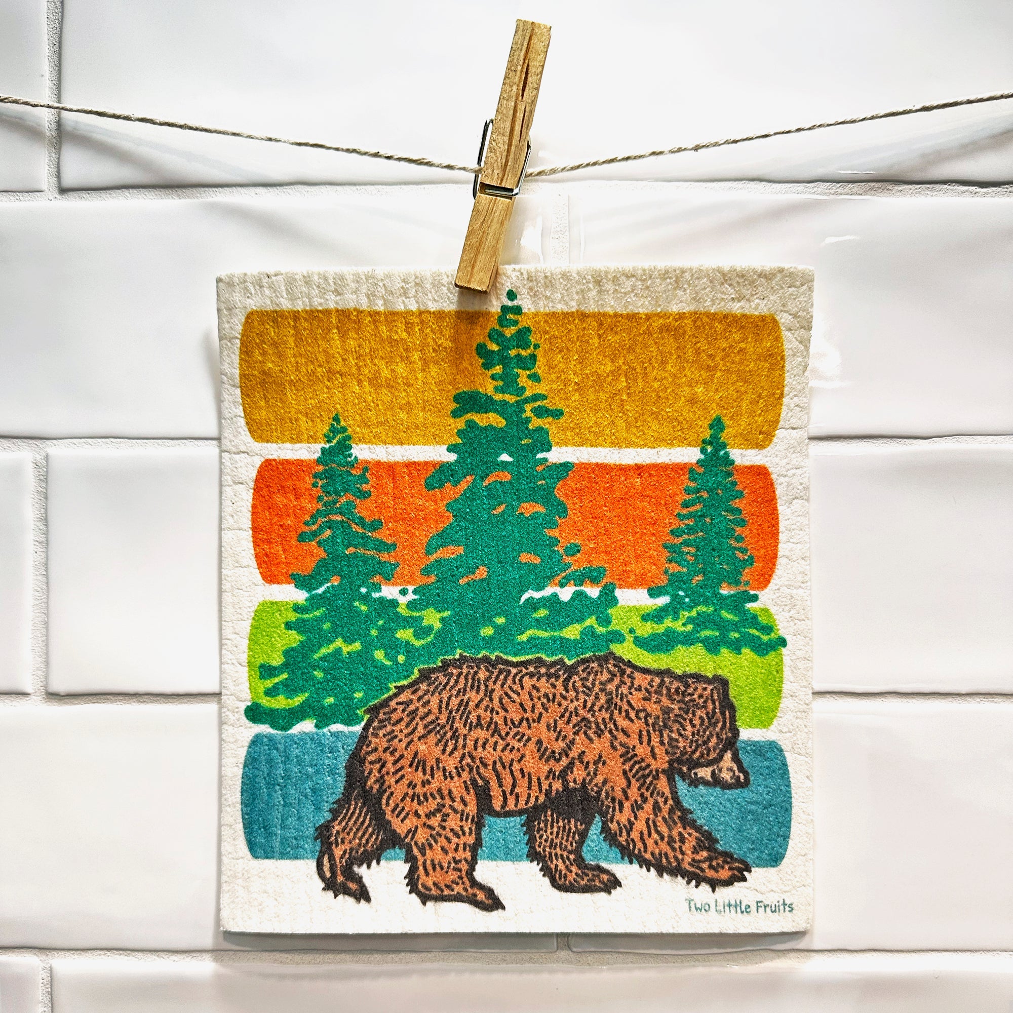 Colorful Forest Bear Swedish dishcloth hanging on a line, featuring a playful bear design among green trees against vibrant stripes.