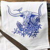 Close-up of a colorful tea towel set featuring a brown bison surrounded by sunflowers, with decorative items scattered around.