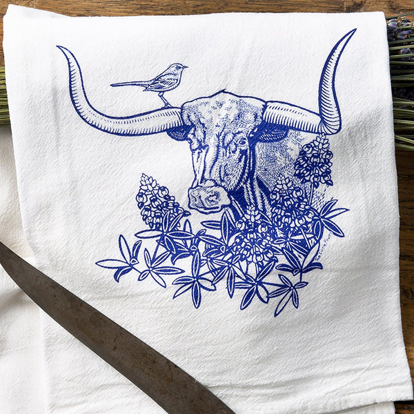 Close-up of a colorful tea towel set featuring a brown bison surrounded by sunflowers, with decorative items scattered around.