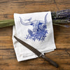 Bright colorful tea towel set showcasing a blue longhorn steer design with flowers, accompanied by lavender and a vintage knife on a rustic wooden table.