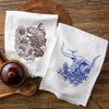 Cheerful colorful tea towel set featuring a brown bison design with sunflowers and a blue longhorn steer with bluebonnets on a wooden surface.
