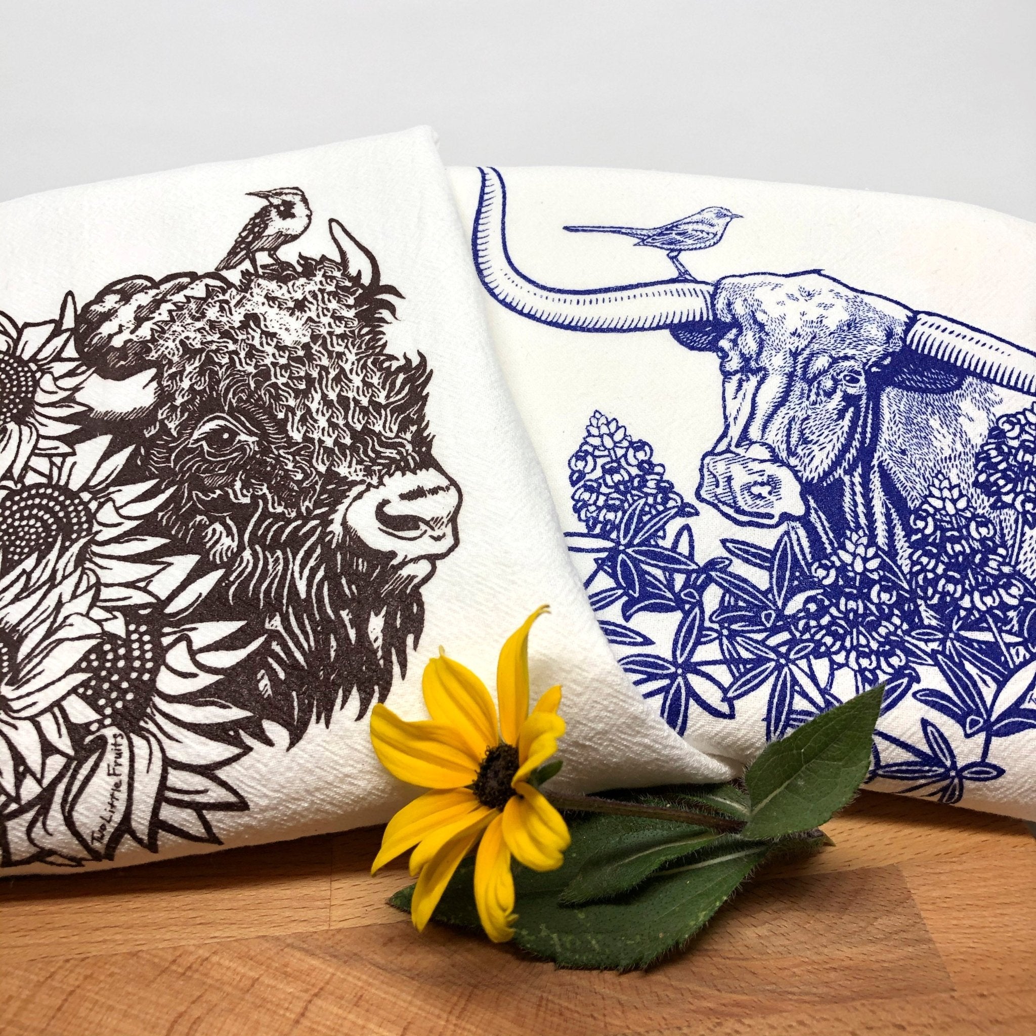 Colorful tea towel set showcasing a brown bison and a blue longhorn steer with a sunflower and a flower arrangement around it.