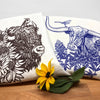 Colorful tea towel set showcasing a brown bison and a blue longhorn steer with a sunflower and a flower arrangement around it.