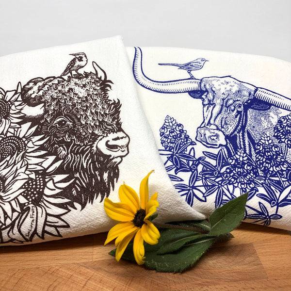 Colorful tea towel set showcasing a brown bison and a blue longhorn steer with a sunflower and a flower arrangement around it.